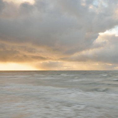 Baltic sea at sunset. Dramatic sky, blue and pink glowing clouds, golden sunlight. Waves, splashing water. Picturesque scenery, seascape, nature. Panoramic view, long exposure