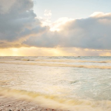 Gün batımında Baltık Denizi. Dramatik gökyüzü, mavi ve pembe parlayan bulutlar, altın güneş ışığı. Dalgalar, su sıçratma. Resimli manzara, deniz manzarası, doğa. Panoramik görünüm, uzun pozlama