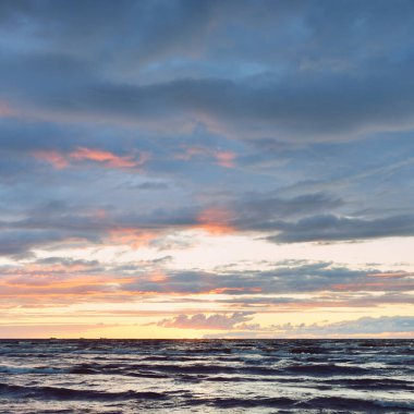 Gün batımında Baltık kıyılarından panoramik manzara. Dramatik fırtına gökyüzü, parlayan bulutlar, altın güneş ışığı. Dalgalar, su sıçratma. Doğa, çevre, kararsız hava