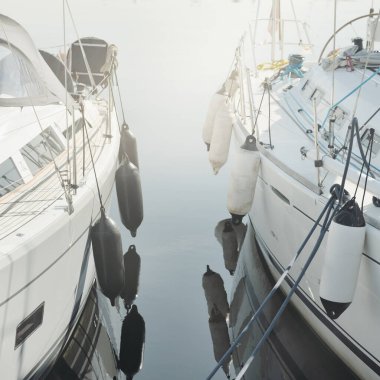 Beyaz modern yelkenli (kiralık ve satılık) yat limanındaki bir rıhtıma demirlemiş. Deniz aracı, ulaşım, amatör yelkencilik, spor, boş zaman aktivitesi, tatiller, gezinti, eğlence kavramları.