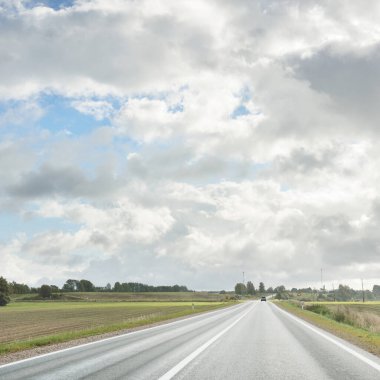 Tarlalar ve orman boyunca (asfalt yol) yol. Arabadan bak. Dramatik fırtına bulutları. Seyahat yerleri, rotalar, tatiller, lojistik, uzak yerler