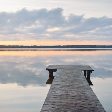 Orman Gölü (nehir) gün batımında. Ahşap iskele. Parlayan bulutlar, durgun ve berrak suda simetri yansımaları. Idyllic manzara. Doğa, ekoloji, ekolojik rezerv, eko-turizm, yürüyüş, tatiller