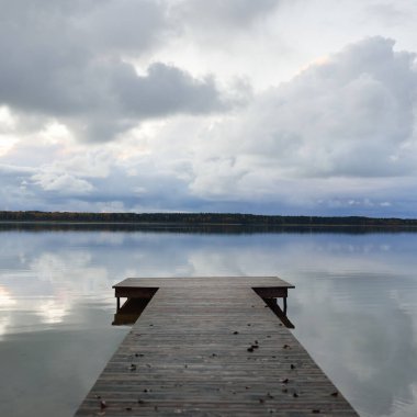 Gün batımında Orman Nehri (Lake). Ahşap iskele. Dramatik gökyüzü, karanlık, parlak bulutlar. Kristal berrak suda simetri yansımaları. Panoramik sonbahar manzarası. Doğa, ekoloji, ekoloji, ekolojik tatil beldesi