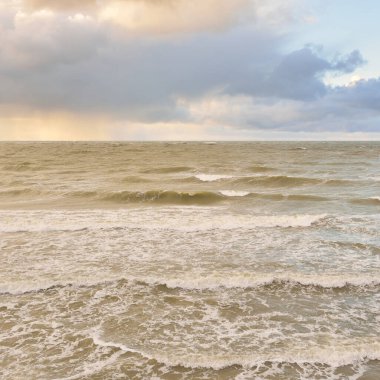 Gün batımında Baltık Denizi. Dramatik gökyüzü, mavi ve pembe parlayan bulutlar, altın güneş ışığı. Dalgalar, su sıçratma. Resimli manzara, deniz manzarası, doğa. Panoramik görünüm, uzun pozlama