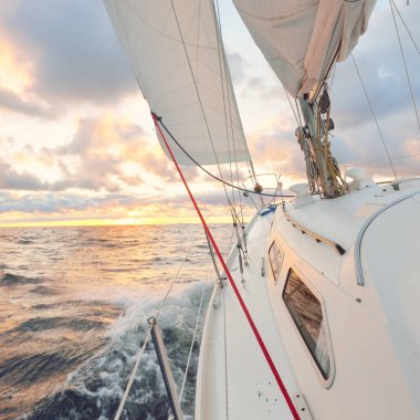 Gün batımında açık denizde yelken açmak. Güvertenin yakın görüntüsü, direk ve yelkenler. Yağmurdan sonra açık gökyüzü, çarpıcı parlayan bulutlar, altın güneş ışığı, dalgalar ve su sıçramaları, kasırga. Destansı deniz manzarası