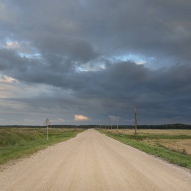 Fırtına sırasında tarımsal tarlalardan ve ormandan geçen boş bir köy yolu. Dramatik gökyüzü, kara bulutlar. Doğa, tatiller, özgürlük, uzak yerler, tehlikeli sürüş, kararsız hava kavramları
