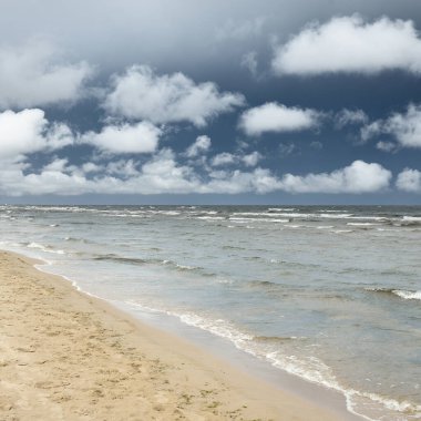 Güneşli bir günde Baltık Denizi kıyısı. Kumsal, kum tepeleri. Fırtınadan sonra dramatik gökyüzü, parlayan bulutlar.. Doğa, tatiller, eğlence. eko turizm