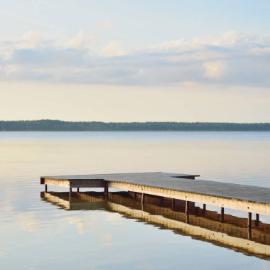 Orman Gölü (nehir) gün batımında. Ahşap iskele. Parlayan bulutlar, durgun ve berrak suda simetri yansımaları. Idyllic manzara. Doğa, ekoloji, ekolojik rezerv, eko-turizm, yürüyüş, tatiller