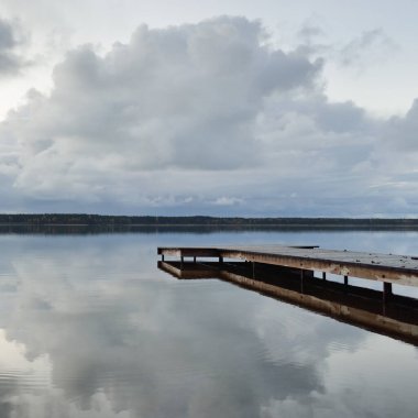 Gün batımında Orman Nehri (Lake). Ahşap iskele. Dramatik gökyüzü, karanlık, parlak bulutlar. Kristal berrak suda simetri yansımaları. Panoramik sonbahar manzarası. Doğa, ekoloji, ekoloji, ekolojik tatil beldesi