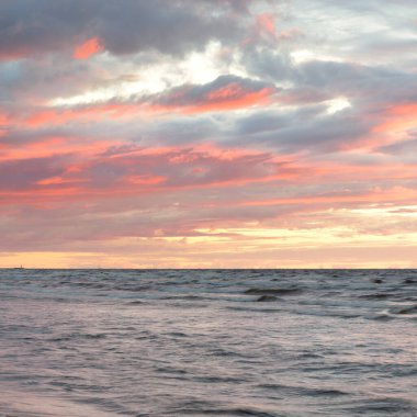 Gün batımında Baltık kıyılarından panoramik manzara. Dramatik fırtına gökyüzü, parlayan bulutlar, altın güneş ışığı. Dalgalar, su sıçratma. Doğa, çevre, kararsız hava