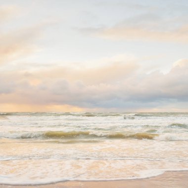 Gün batımında Baltık Denizi. Dramatik gökyüzü, mavi ve pembe parlayan bulutlar, altın güneş ışığı. Dalgalar, su sıçratma. Resimli manzara, deniz manzarası, doğa. Panoramik görünüm, uzun pozlama
