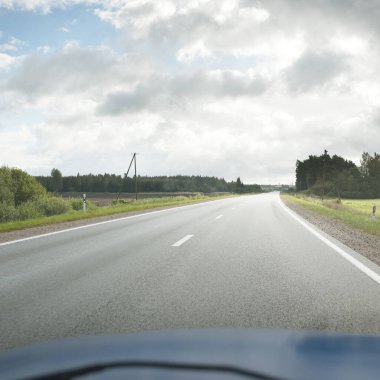 Tarlalar ve orman boyunca (asfalt yol) yol. Arabadan bak. Dramatik fırtına bulutları. Seyahat yerleri, rotalar, tatiller, lojistik, uzak yerler