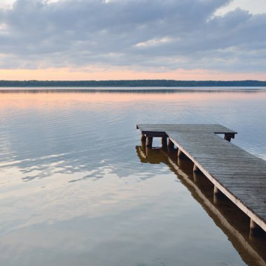 Orman Gölü (nehir) gün batımında. Ahşap iskele. Parlayan bulutlar, durgun ve berrak suda simetri yansımaları. Idyllic manzara. Doğa, ekoloji, ekolojik rezerv, eko-turizm, yürüyüş, tatiller