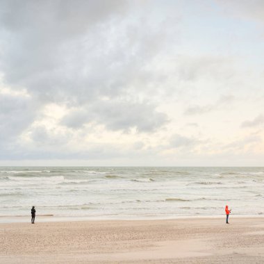 Baltic sea shore at sunset. Beach, sand dunes. Clear sunset sky, glowing clouds. Lonely people walking with a mobile phones. Local travel, eco tourism, mental health, social issues and distance themes