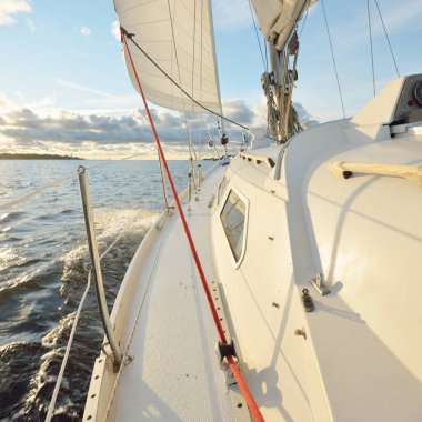 Gün batımında açık denizde yelken açmak. Güvertenin yakın görüntüsü, direk ve yelkenler. Yağmurdan sonra açık gökyüzü, çarpıcı parlayan bulutlar, altın güneş ışığı, dalgalar ve su sıçramaları, kasırga. Destansı deniz manzarası