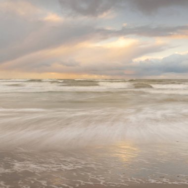 Gün batımında Baltık Denizi. Dramatik gökyüzü, mavi ve pembe parlayan bulutlar, altın güneş ışığı. Dalgalar, su sıçratma. Resimli manzara, deniz manzarası, doğa. Panoramik görünüm, uzun pozlama