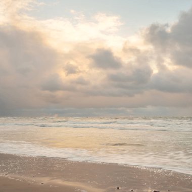 Gün batımında Baltık Denizi. Dramatik gökyüzü, mavi ve pembe parlayan bulutlar, altın güneş ışığı. Dalgalar, su sıçratma. Resimli manzara, deniz manzarası, doğa. Panoramik görünüm, uzun pozlama