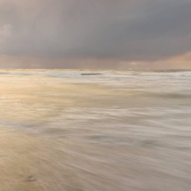 Gün batımında Baltık Denizi. Dramatik gökyüzü, mavi ve pembe parlayan bulutlar, altın güneş ışığı. Dalgalar, su sıçratma. Resimli manzara, deniz manzarası, doğa. Panoramik görünüm, uzun pozlama