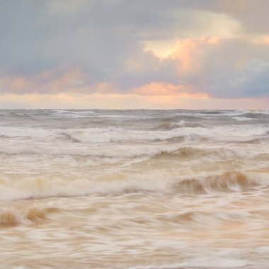 Baltic sea at sunset. Dramatic sky, blue and pink glowing clouds, golden sunlight. Waves, splashing water. Picturesque scenery, seascape, nature. Panoramic view, long exposure
