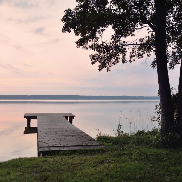 Forest lake at sunset. Wooden pier. Soft sunlight, glowing clouds, symmetry reflections in a crystal clear water. Idyllic landscape. Panoramic view. Nature, ecology, ecotourism. Peace and joy concepts