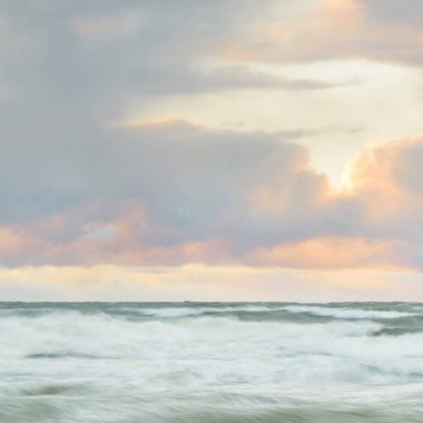 Gün batımında Baltık Denizi. Dramatik gökyüzü, mavi ve pembe parlayan bulutlar, altın güneş ışığı. Dalgalar, su sıçratma. Resimli manzara, deniz manzarası, doğa. Panoramik görünüm, uzun pozlama