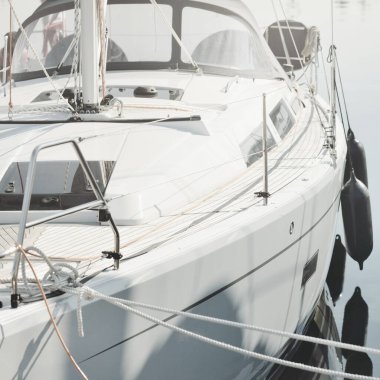 White modern sailboat (for rent and sale) moored to a pier in a yacht marina. Wooden teak deck. Nautical vessel, transportation, amateur sailing, vacations, cruising, recreation concepts