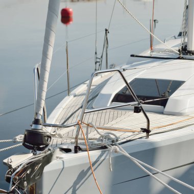 White modern sailboat (for rent and sale) moored to a pier in a yacht marina. Wooden teak deck. Nautical vessel, transportation, amateur sailing, vacations, cruising, recreation concepts