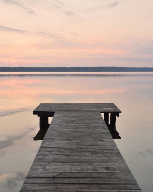Forest lake at sunset. Wooden pier. Soft sunlight, glowing clouds, symmetry reflections in a crystal clear water. Idyllic landscape. Panoramic view. Nature, ecology, ecotourism, swimming, fishing
