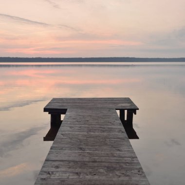 Forest lake at sunset. Wooden pier. Soft sunlight, glowing clouds, symmetry reflections in a crystal clear water. Idyllic landscape. Panoramic view. Nature, ecology, ecotourism, swimming, fishing