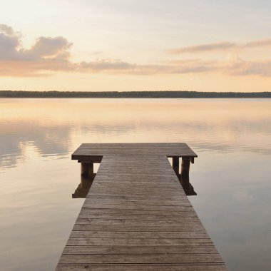 Forest lake (river) at sunset. Wooden pier. Glowing clouds, symmetry reflections in a still crystal clear water. Idyllic landscape. Nature, ecology, ecological reserve, ecotourism, hiking, vacations