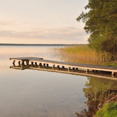 Orman Gölü (nehir) gün batımında. Ahşap iskele. Parlayan bulutlar, durgun ve berrak suda simetri yansımaları. Idyllic manzara. Doğa, ekoloji, ekolojik rezerv, eko-turizm, yürüyüş, tatiller