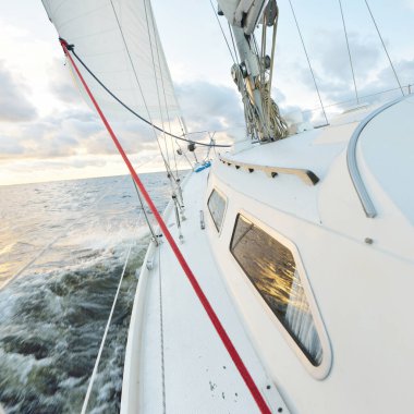 Gün batımında açık denizde yelken açmak. Güvertenin yakın görüntüsü, direk ve yelkenler. Yağmurdan sonra açık gökyüzü, çarpıcı parlayan bulutlar, altın güneş ışığı, dalgalar ve su sıçramaları, kasırga. Destansı deniz manzarası