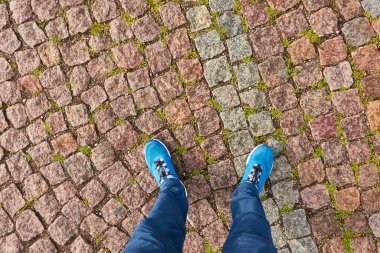 Çakıl taşı yolunda duran bir adam. Mavi kot pantolon ve yürüyüş botları. Doku, arka plan, duvar kağıdı. Seyahat, turizm, yürüyüş, bisiklet. Şehir ve peyzaj tasarımının ayrıntıları. Panoramik görünüm
