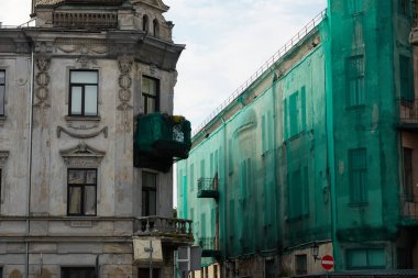 Letonya, Ventspils 'te boş bir cadde. Yeşil bir ağ ile kaplı eski bir ev. Şehir manzarası kavramı. Kentsel planlama, dış yapı, yenileme, onarım, restorasyon, iş alanı güvenliği temaları