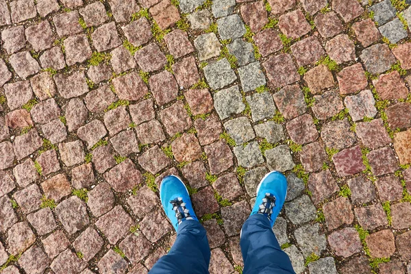 Man standing on cobblestone road. Blue jeans and trekking boots. Texture, background, wallpaper. Travel, tourism, walking, cycling. Details of urban and landscaping design. Panoramic view