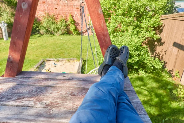 Man Resting Wooden Swing Bench Foam Clogs Blue Jeans Backyard — Stock Photo, Image