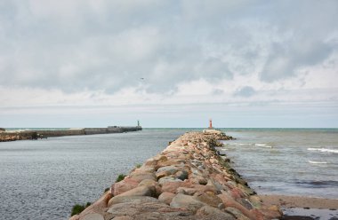Baltık kıyıları (kum tepeleri, plaj). Dramatik gökyüzü, parlayan bulutlar. Deniz fenerine doğru ilerleyin, dalgalar yakın çekim yapsın. Doğa, çevre, ekoloji, eko-turizm, yürüyüş, keşif teması. Letonya