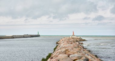 Baltık kıyıları (kum tepeleri, plaj). Dramatik gökyüzü, parlayan bulutlar. Deniz fenerine doğru ilerleyin, dalgalar yakın çekim yapsın. Doğa, çevre, ekoloji, eko-turizm, yürüyüş, keşif teması. Letonya