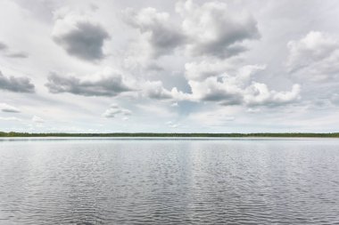 Kristal berrak bir orman gölü (nehir) kıyısından panoramik manzara. Dramatik gökyüzü, parlayan fırtına bulutları. Idyllic manzara. İlkbahar, yazın başı. Doğa, çevre, ekoloji, eko-turizm, yürüyüş