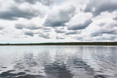 Kristal berrak bir orman gölü (nehir) kıyısından panoramik manzara. Dramatik gökyüzü, parlayan fırtına bulutları. Idyllic manzara. İlkbahar, yazın başı. Doğa, çevre, ekoloji, eko-turizm, yürüyüş