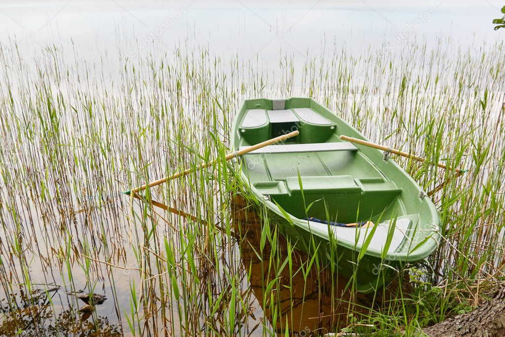 Small green boat anchored in forest lake. Scandinavia. Transportation, traditional craft, recreation, leisure activity, healthy lifestyle, local tourism, sport, rowing, hiking, summer vacations themes