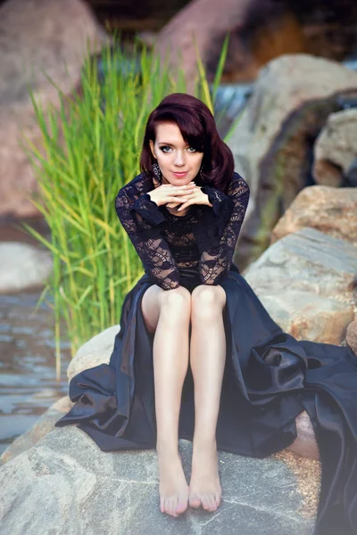 Nádherná dívka v černé krajkové šaty sedí na skále — Stock fotografie