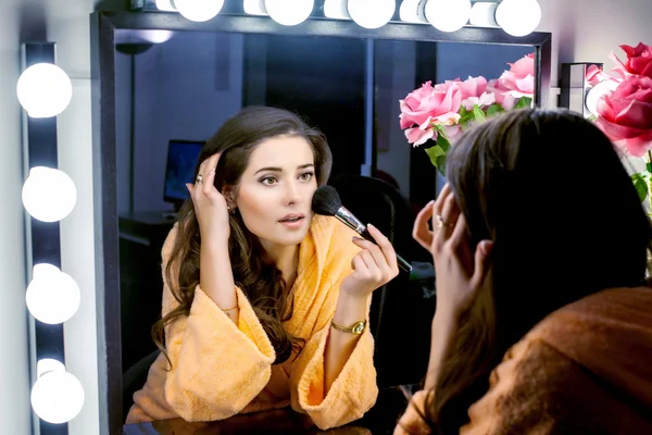 Woman in orange robe doing her makeup and wathching in mirror — Stock Photo, Image