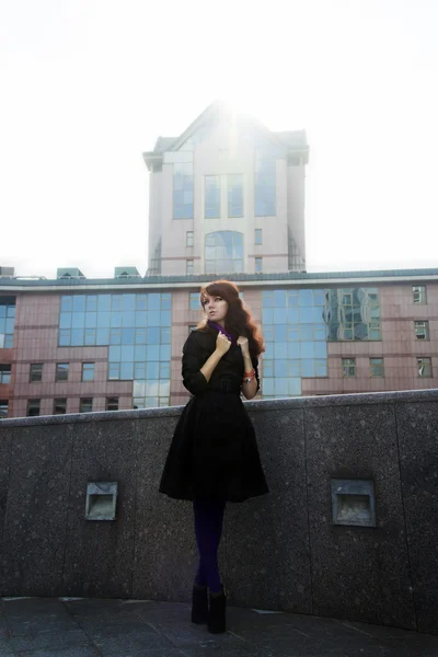 Young woman standing in black coat on urban background — Stock Photo, Image