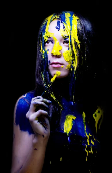 Красота моды крупным планом портрет женщины, выкрашенный в синий и желтый с кисточками и краской на черном фоне — стоковое фото