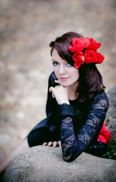 Modeporträt einer Frau in schwarzer Spitze mit roten Blumen auf Steinhintergrund — Stockfoto