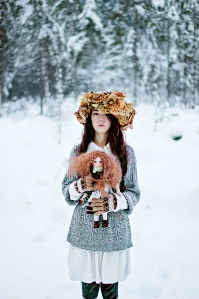 Лесная женщина с осенними листьями и куклой в белом снегу зимой — стоковое фото