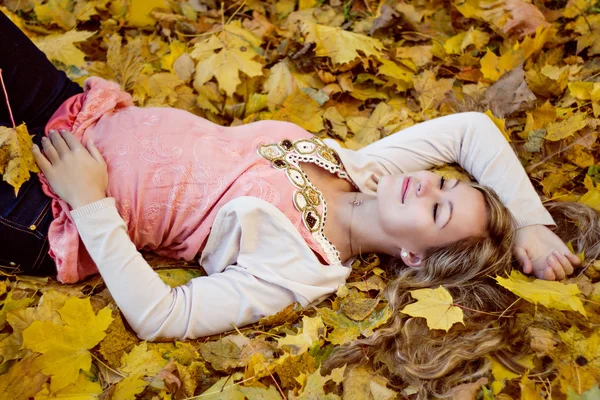 Hermosa mujer embarazada feliz acostada con hojas de otoño — Foto de Stock