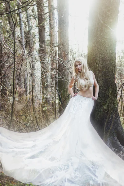 Ange mariée blonde en longue jupe blanche debout dans la forêt ensoleillée — Photo