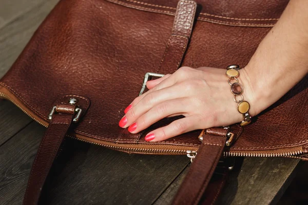 Female hand with bracelet holds a brown leather bag — Stock Photo, Image